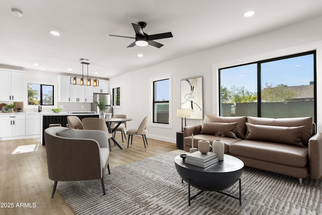 living area featuring ceiling fan with notable chandelier, light wood-style flooring, and recessed lighting