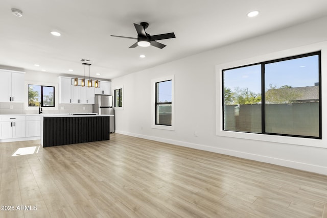 unfurnished living room featuring recessed lighting, baseboards, a sink, and light wood finished floors