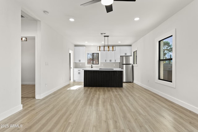 kitchen with light wood-style floors, a kitchen island, white cabinets, and freestanding refrigerator