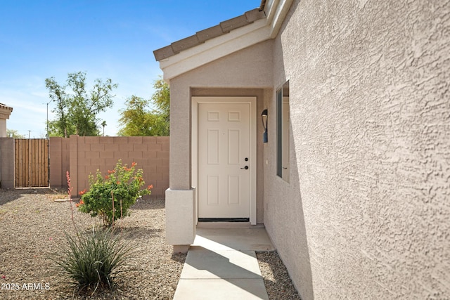 view of exterior entry featuring stucco siding and fence
