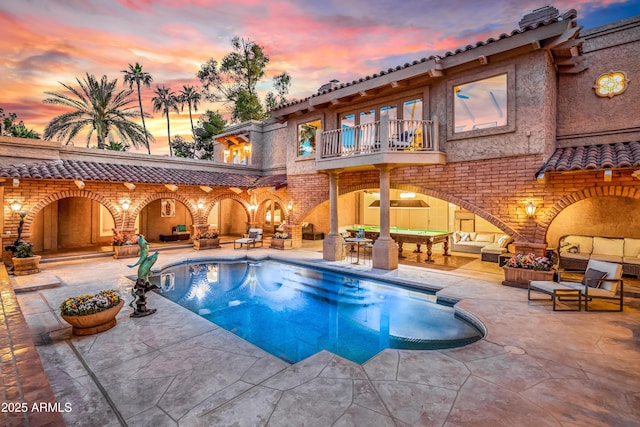 pool at dusk with an outdoor living space and a patio area