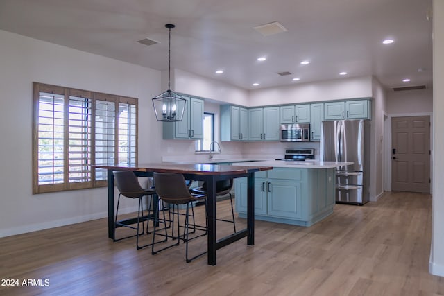 kitchen with a kitchen island, hanging light fixtures, gray cabinetry, appliances with stainless steel finishes, and light hardwood / wood-style floors