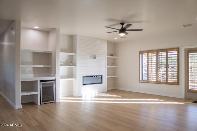 unfurnished living room featuring wine cooler, a large fireplace, ceiling fan, light hardwood / wood-style flooring, and built in features