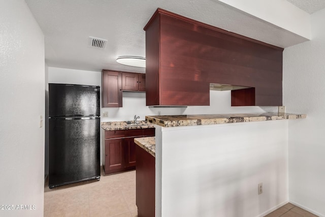 kitchen featuring kitchen peninsula, black refrigerator, a textured ceiling, and light stone countertops