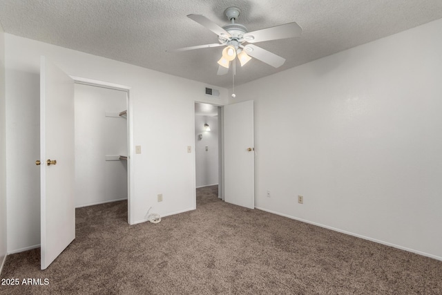 unfurnished bedroom featuring a spacious closet, a textured ceiling, dark carpet, a closet, and ceiling fan