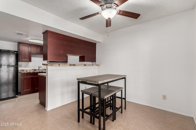 kitchen with kitchen peninsula, black fridge, a textured ceiling, and light tile patterned flooring