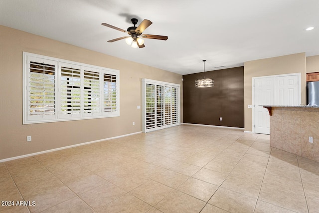 tiled empty room with ceiling fan with notable chandelier