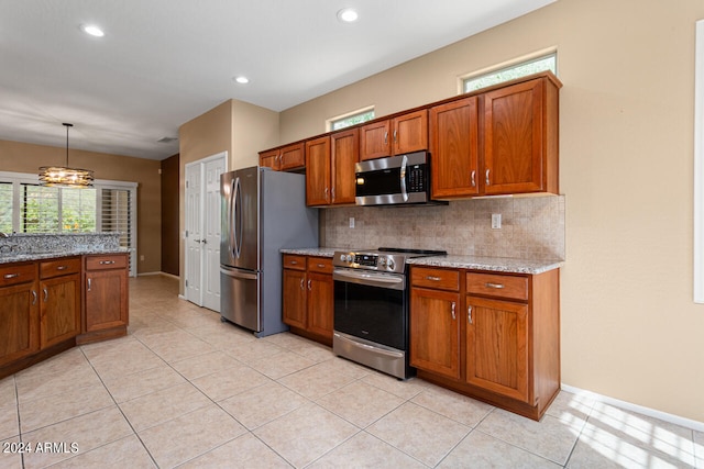 kitchen with light stone counters, appliances with stainless steel finishes, hanging light fixtures, and light tile patterned flooring