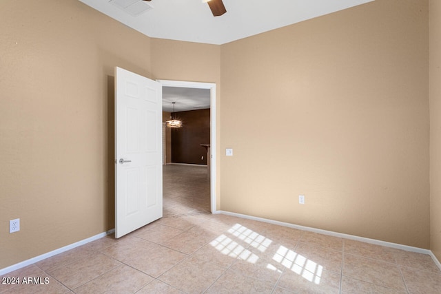 tiled spare room with ceiling fan with notable chandelier