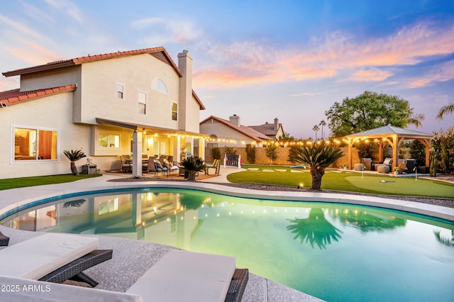 pool at dusk with a gazebo, an outdoor hangout area, and a patio area