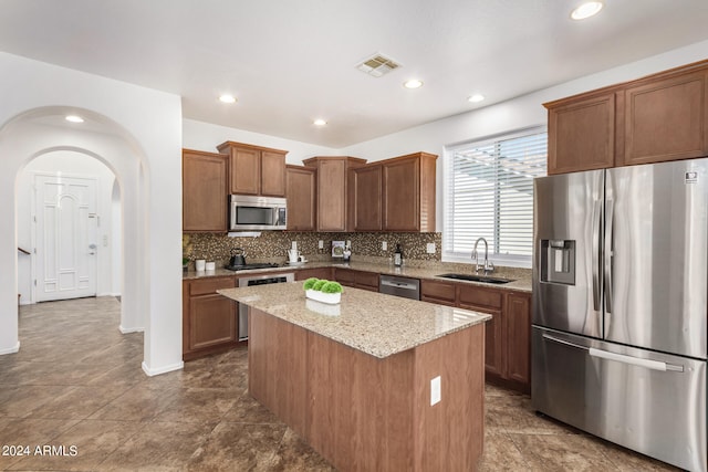 kitchen with sink, light stone counters, backsplash, a kitchen island, and appliances with stainless steel finishes