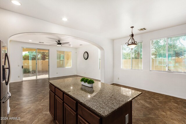 kitchen with light stone countertops, stainless steel fridge, ceiling fan, a center island, and hanging light fixtures