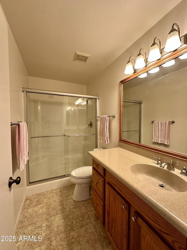 bathroom with a shower with door, vanity, a textured ceiling, and toilet