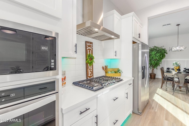 kitchen featuring light wood finished floors, stainless steel appliances, light countertops, visible vents, and wall chimney range hood