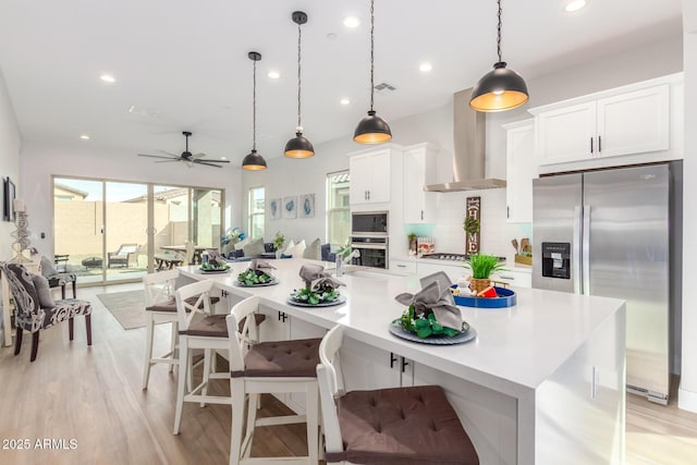 kitchen with tasteful backsplash, light countertops, appliances with stainless steel finishes, white cabinetry, and wall chimney exhaust hood