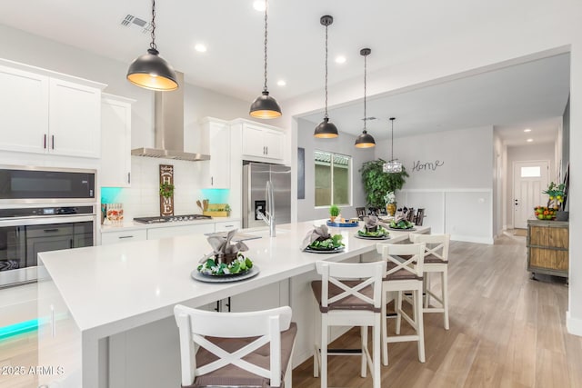 kitchen with decorative backsplash, wall chimney exhaust hood, stainless steel appliances, light countertops, and a large island with sink