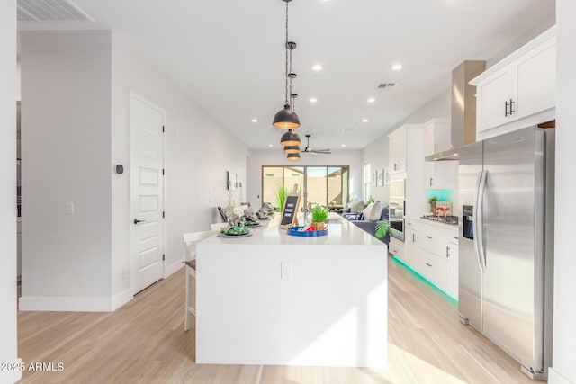 kitchen with appliances with stainless steel finishes, visible vents, a kitchen island, and wall chimney exhaust hood