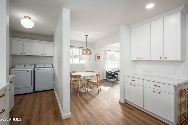 clothes washing area featuring separate washer and dryer, light hardwood / wood-style flooring, and cabinets