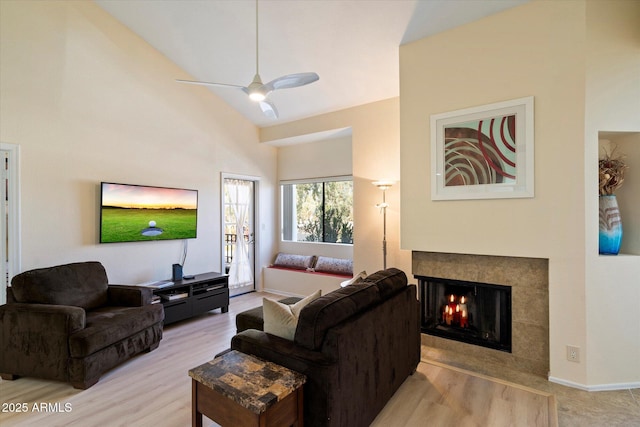 living room featuring a tiled fireplace, ceiling fan, high vaulted ceiling, and light hardwood / wood-style flooring