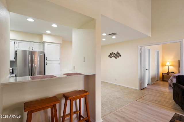 kitchen with stainless steel refrigerator, white cabinetry, a kitchen bar, kitchen peninsula, and light hardwood / wood-style flooring