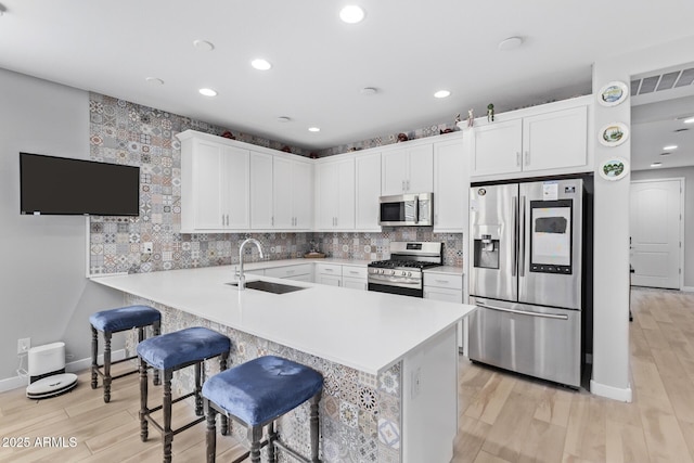 kitchen with appliances with stainless steel finishes, white cabinetry, sink, a breakfast bar area, and kitchen peninsula