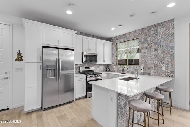 kitchen with a breakfast bar, sink, kitchen peninsula, stainless steel appliances, and white cabinets