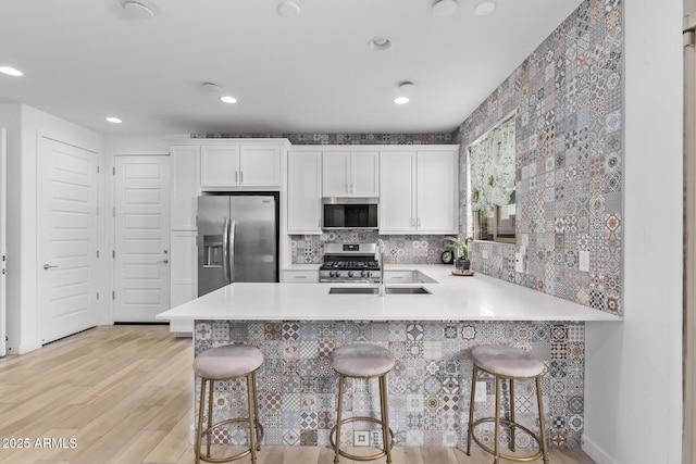 kitchen with white cabinetry, a kitchen breakfast bar, kitchen peninsula, stainless steel appliances, and light hardwood / wood-style floors