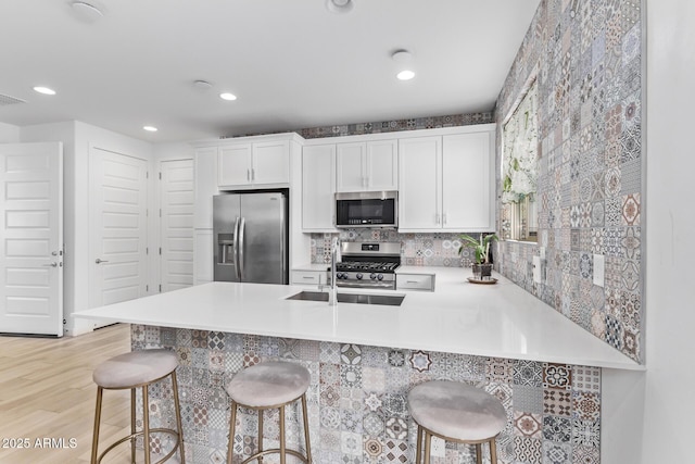 kitchen featuring appliances with stainless steel finishes, sink, white cabinets, a kitchen bar, and kitchen peninsula