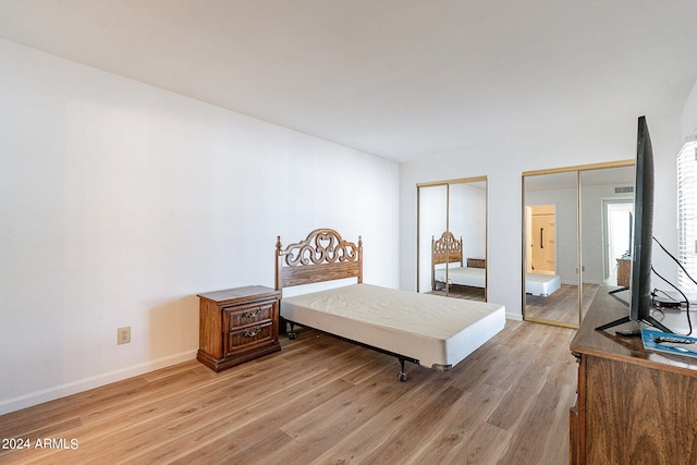 bedroom with baseboards, light wood-style floors, and two closets