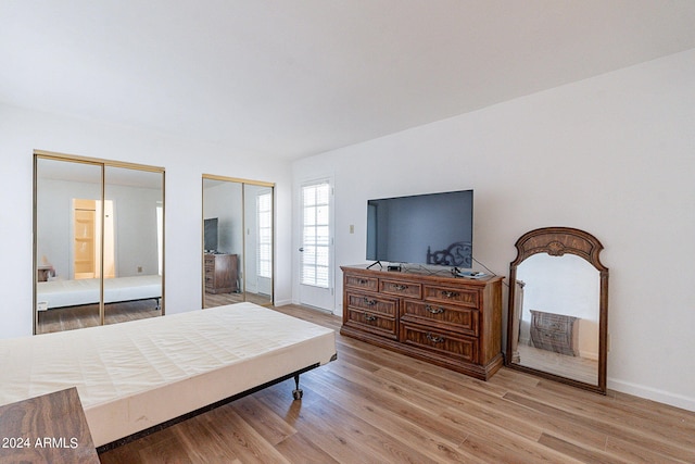 bedroom with baseboards, light wood-type flooring, and two closets
