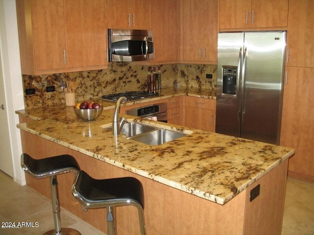 kitchen featuring light stone counters, appliances with stainless steel finishes, a breakfast bar, tasteful backsplash, and kitchen peninsula