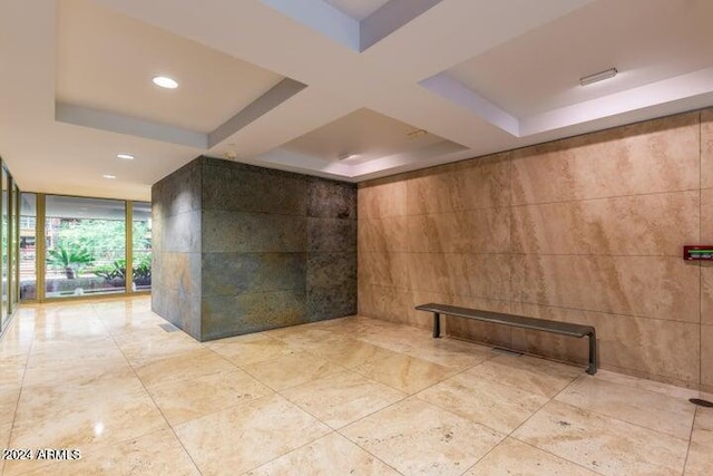 tiled spare room featuring coffered ceiling, tile walls, a raised ceiling, and expansive windows