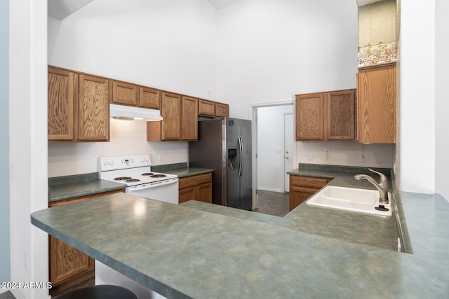 kitchen featuring sink, a high ceiling, kitchen peninsula, white range with electric cooktop, and stainless steel fridge