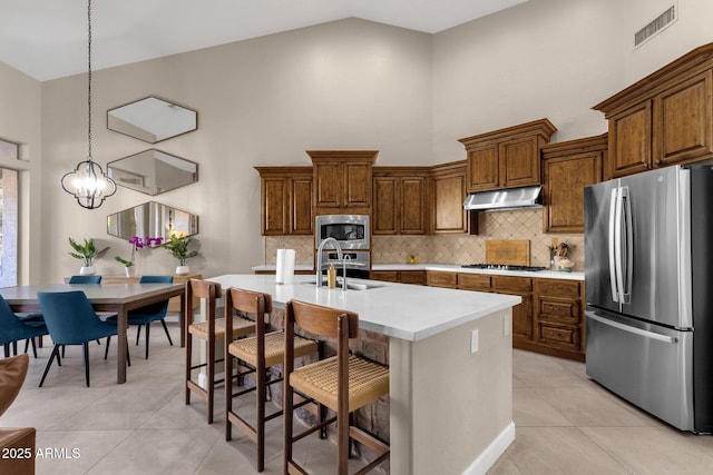 kitchen with stainless steel appliances, tasteful backsplash, a kitchen breakfast bar, a kitchen island with sink, and high vaulted ceiling