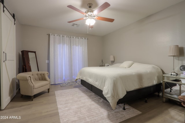 bedroom featuring a barn door, ceiling fan, and light hardwood / wood-style flooring