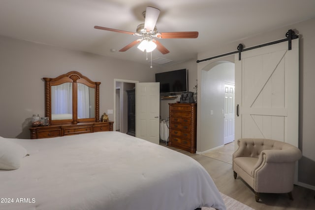 bedroom with a barn door, ceiling fan, a closet, and light hardwood / wood-style floors