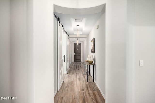 corridor with a barn door and light hardwood / wood-style floors