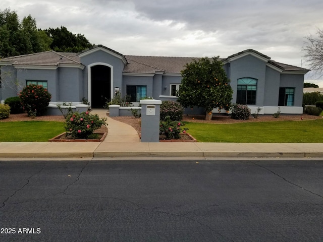 mediterranean / spanish home featuring a tiled roof, a front lawn, and stucco siding