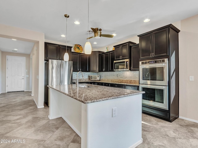 kitchen with ceiling fan, hanging light fixtures, stainless steel appliances, tasteful backsplash, and an island with sink