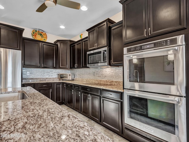 kitchen with dark brown cabinetry, ceiling fan, light stone counters, backsplash, and appliances with stainless steel finishes