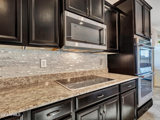 kitchen with decorative backsplash, appliances with stainless steel finishes, light stone counters, dark brown cabinets, and light tile patterned floors