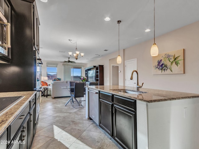 kitchen with sink, hanging light fixtures, ceiling fan, dark stone countertops, and an island with sink