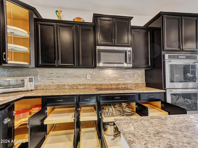 kitchen featuring dark brown cabinetry, light stone countertops, backsplash, and appliances with stainless steel finishes