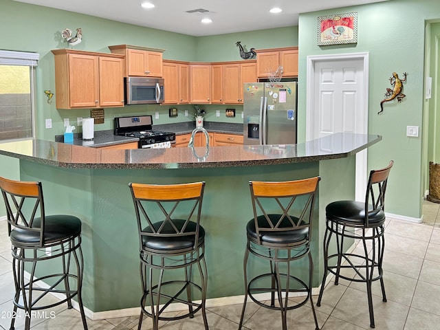 kitchen featuring a breakfast bar, an island with sink, light tile patterned flooring, and appliances with stainless steel finishes