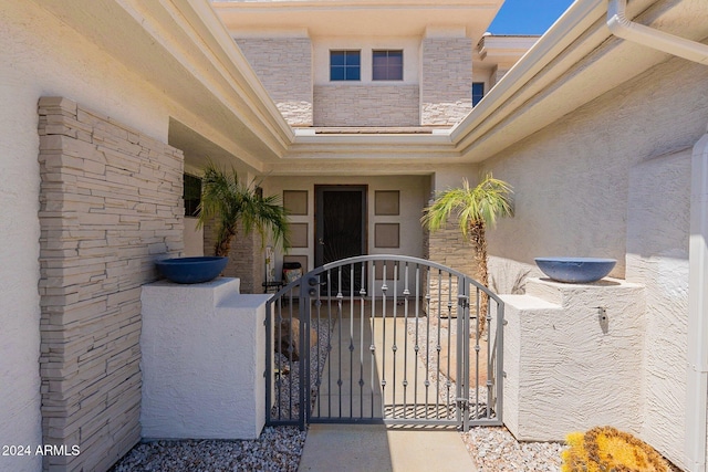 property entrance featuring stone siding, a gate, and stucco siding