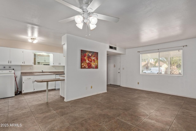 unfurnished living room with visible vents, baseboards, a sink, ceiling fan, and washer / dryer