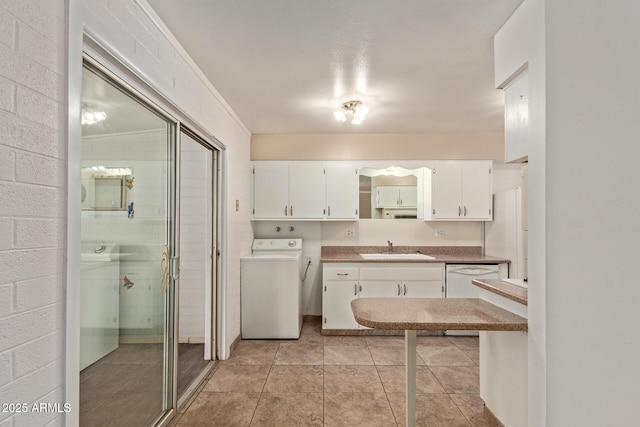 interior space featuring washer / clothes dryer, light tile patterned floors, white dishwasher, a sink, and white cabinetry