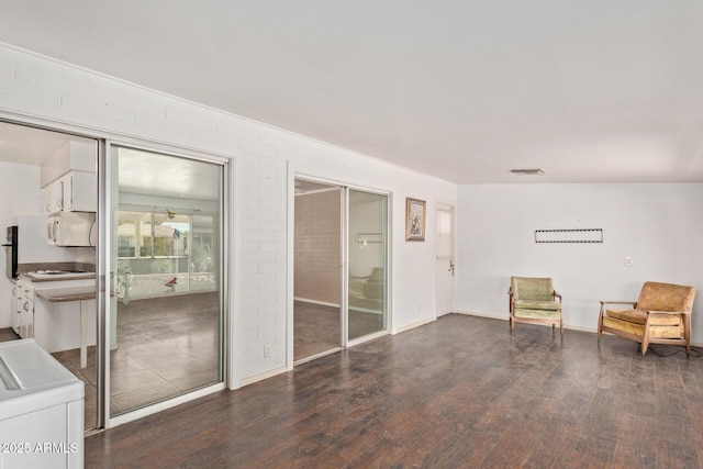 unfurnished room featuring dark wood-style flooring, visible vents, washer / dryer, and brick wall