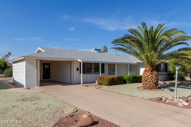 ranch-style home with an attached carport, roof with shingles, driveway, and board and batten siding