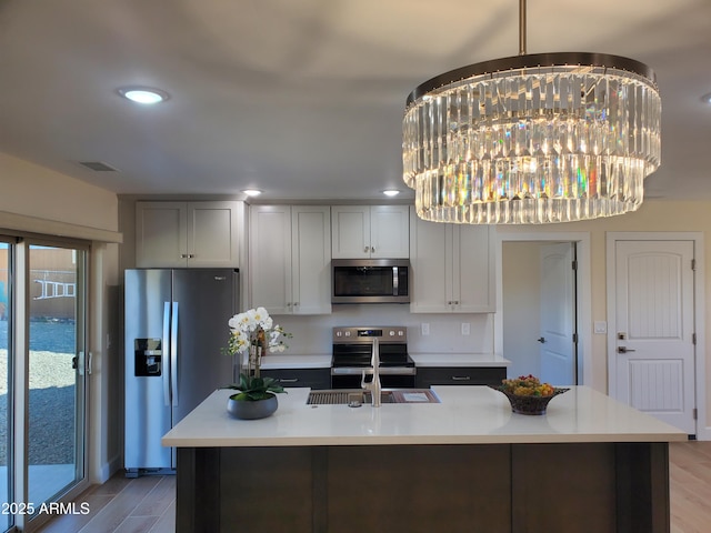 kitchen with a chandelier, light hardwood / wood-style floors, a kitchen island with sink, and stainless steel appliances